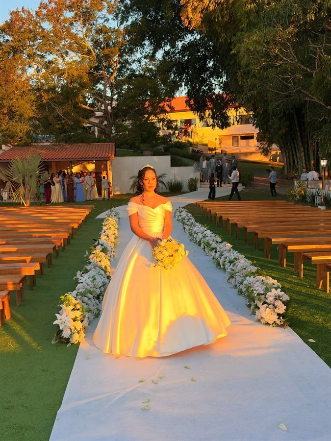 Debutante descendo o corredor de flores iluminado ao anoitecer