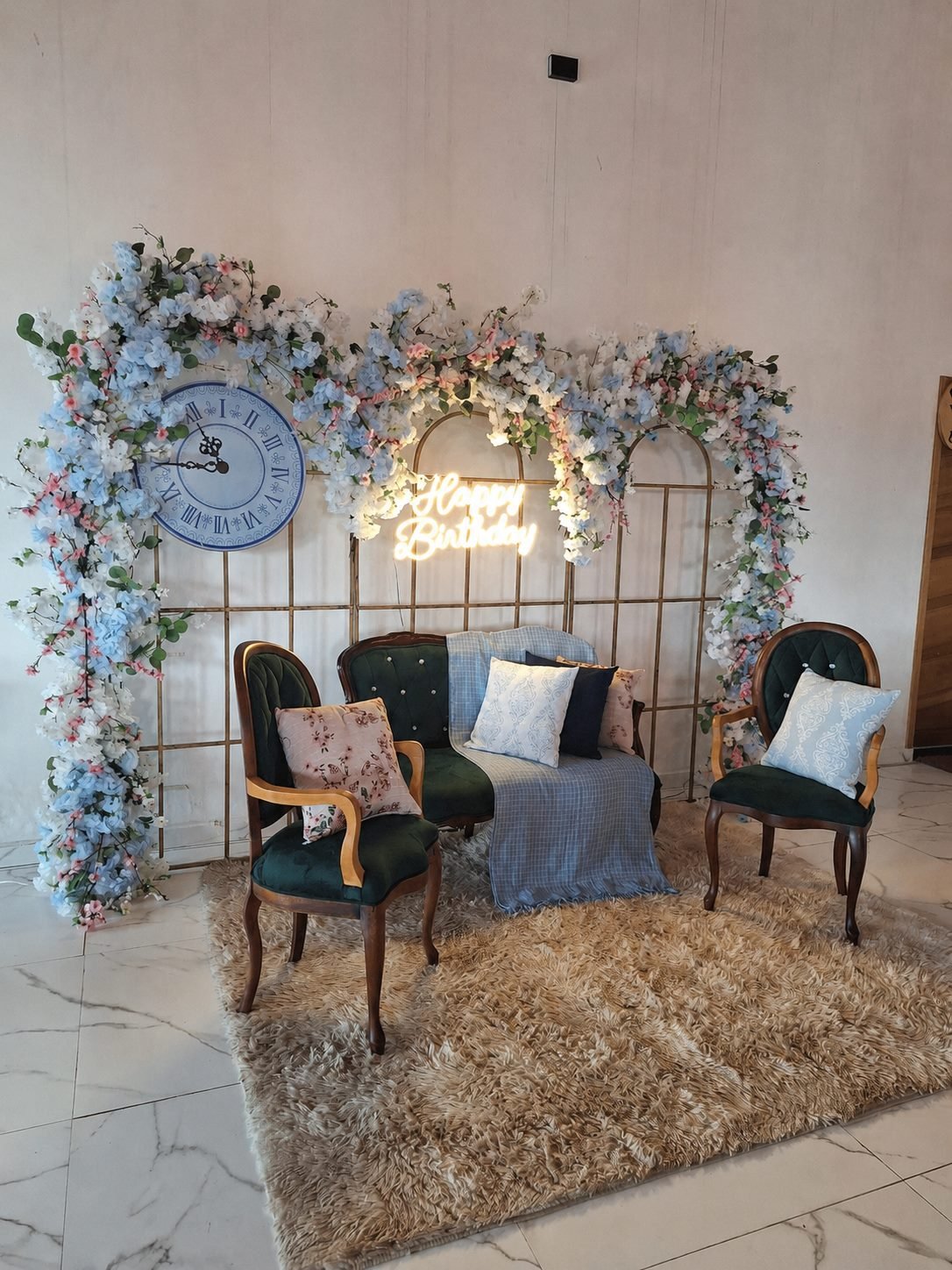 Lounge decorado com painel floral, poltronas verdes e almofadas