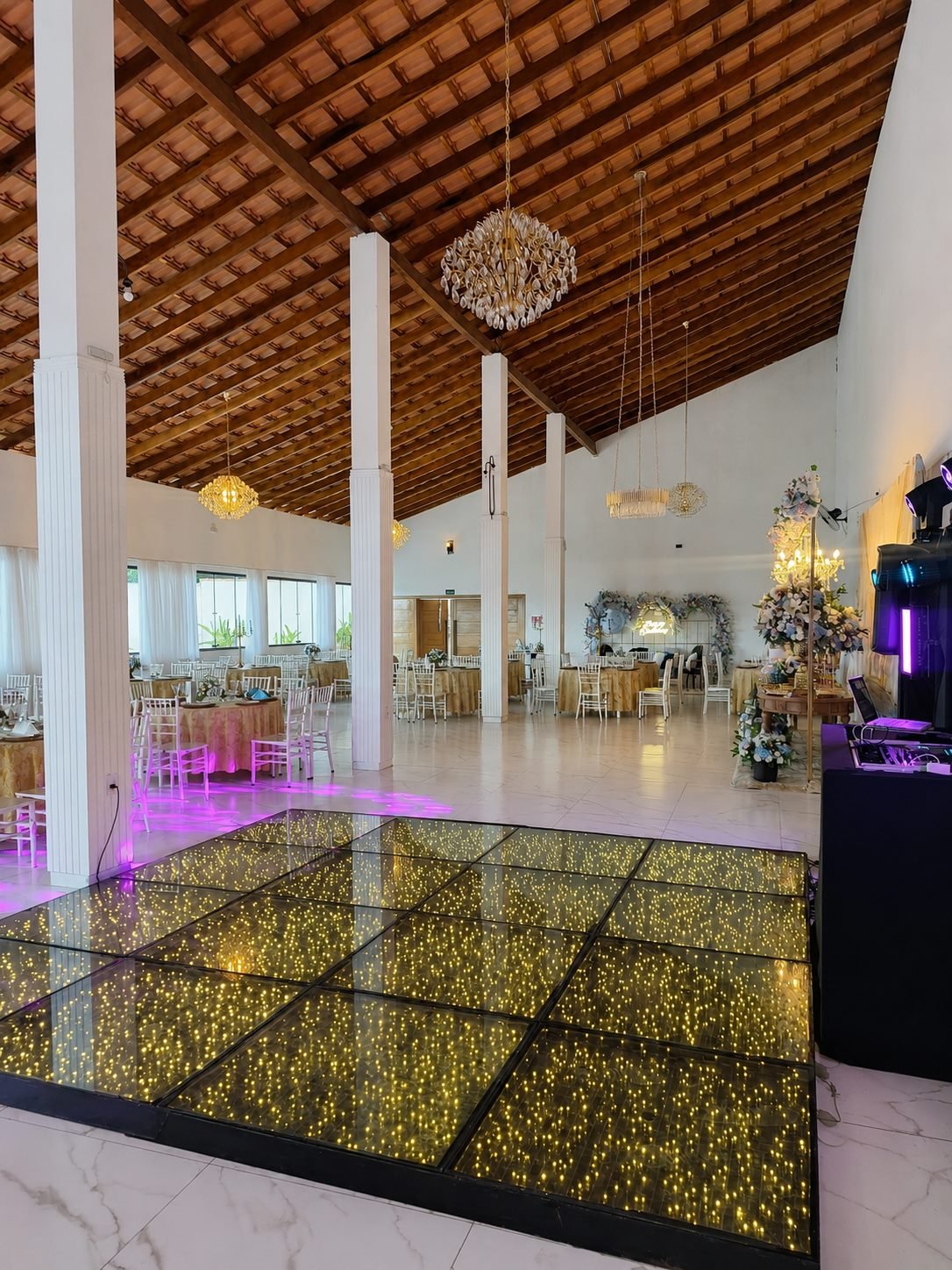 Salão com pista de dança espelhada iluminada e pé-direito alto de madeira