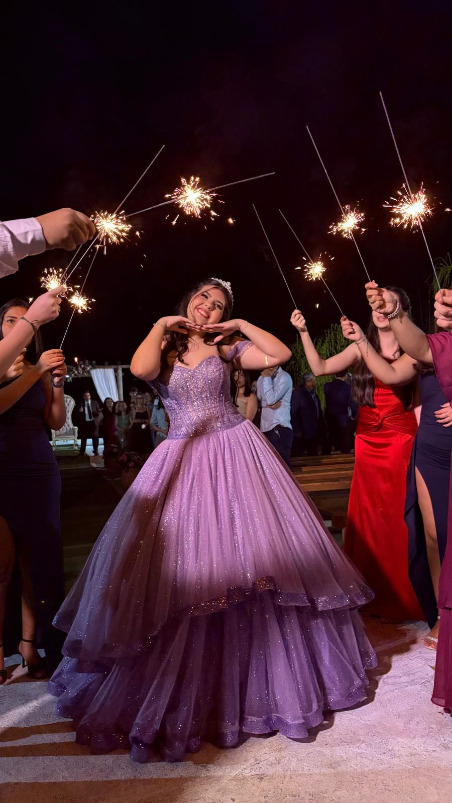 Aniversariante de vestido lilás cercada por convidados com fogos frios