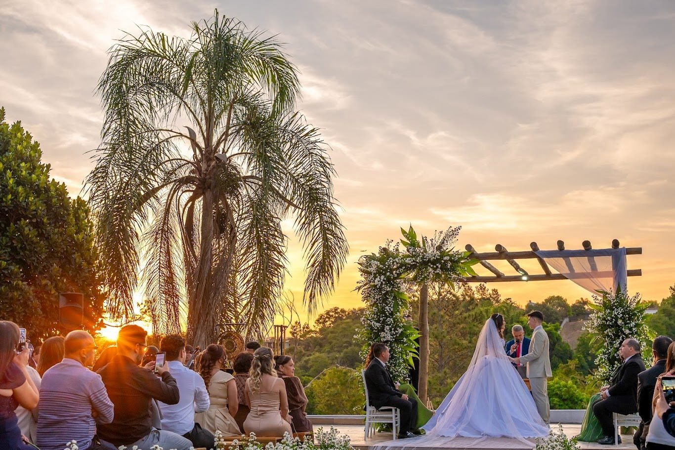 Cerimônia ao pôr do sol com a noiva no altar e a luz dourada atrás das palmeiras